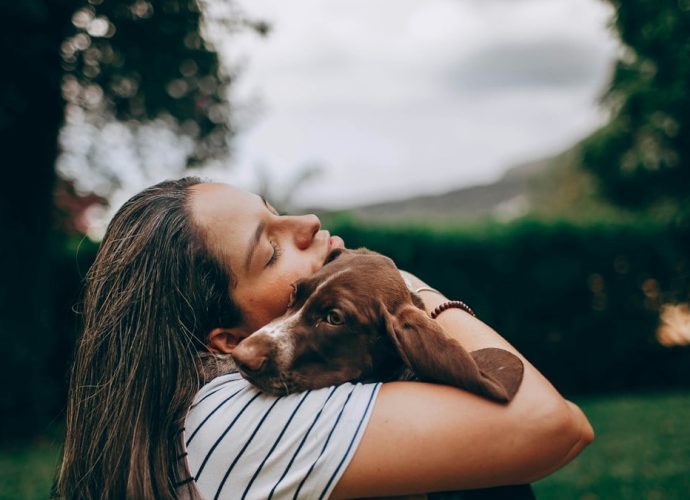 woman in white and black stripe shirt hugging brown short coated dog