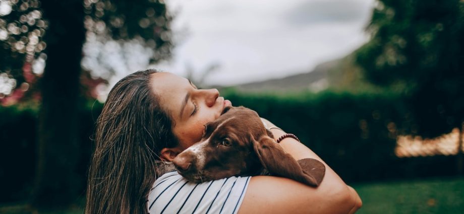 woman in white and black stripe shirt hugging brown short coated dog