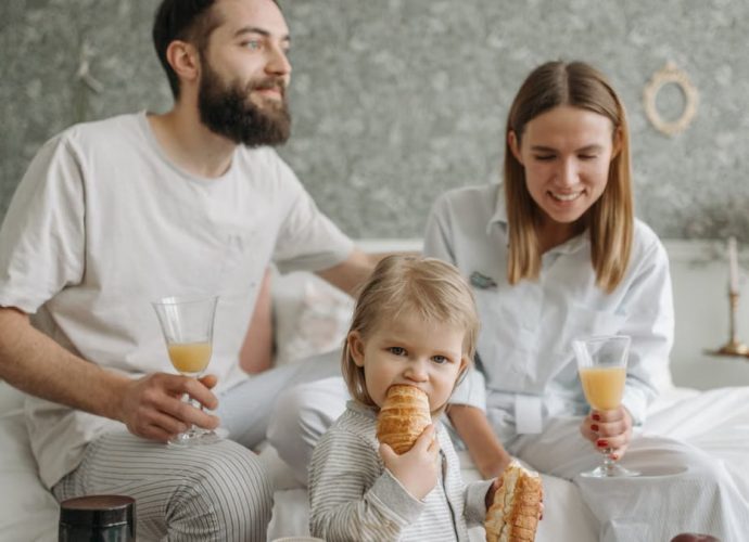 A family enjoying breakfast in their bedroom, featuring croissants and orange juice.