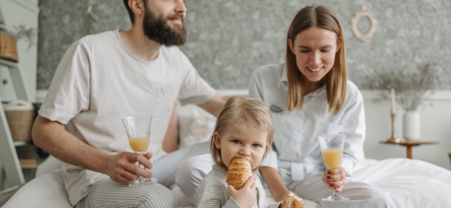 A family enjoying breakfast in their bedroom, featuring croissants and orange juice.